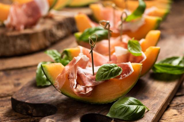 Tranches de melon servies avec du jambon et des feuilles de basilic